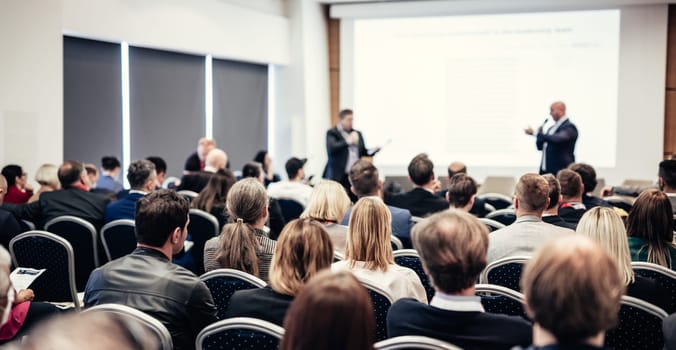 I have a question. Group of business people sitting at the chairs in conference hall. Businessman standing up asking a question. Conference and Presentation. Business and Entrepreneurship.