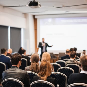 Speaker giving a talk in conference hall at business event. Rear view of unrecognizable people in audience at the conference hall. Business and entrepreneurship concept