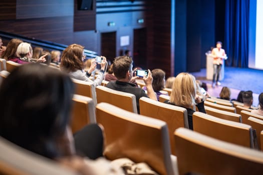 Speaker giving a talk in conference hall at business event. Rear view of unrecognizable people in audience at the conference hall. Business and entrepreneurship concept