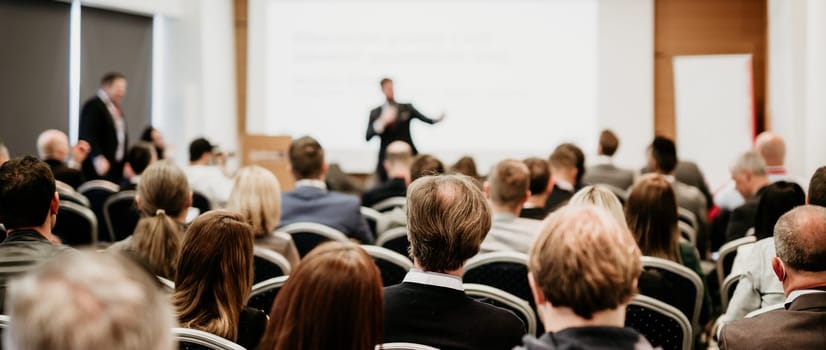 Speaker giving a talk in conference hall at business event. Rear view of unrecognizable people in audience at the conference hall. Business and entrepreneurship concept