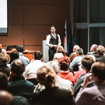 Speaker giving a talk in conference hall at business meeting event. Rear view of unrecognizable people in audience at the conference hall. Business and entrepreneurship concept.