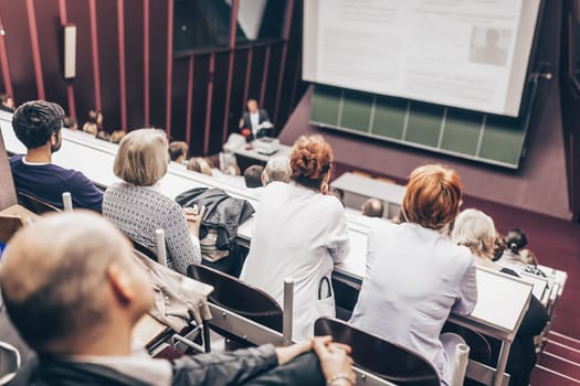 Lecturer at university. Healthcare expert giving a talk to medical faculty professors. Participants listening to lecture and making notes.
