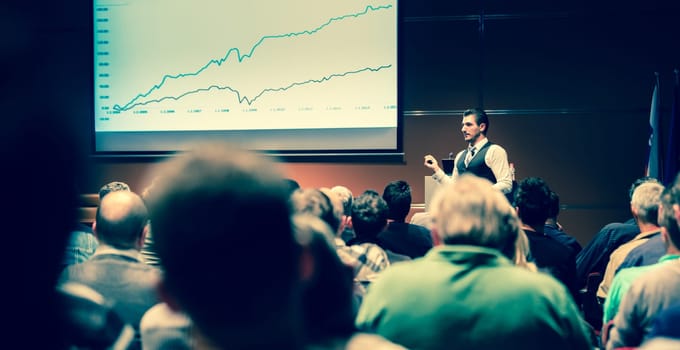 Speaker giving a talk in conference hall at business meeting event. Rear view of unrecognizable people in audience at the conference hall. Business and entrepreneurship concept.