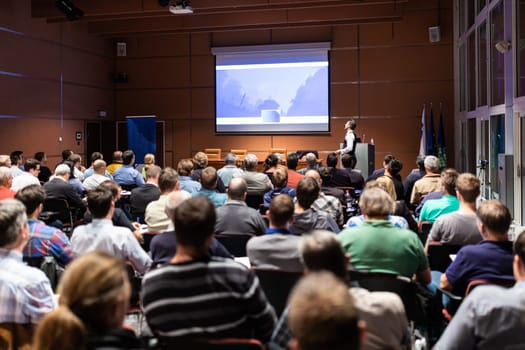Speaker giving a talk in conference hall at business meeting event. Rear view of unrecognizable people in audience at the conference hall. Business and entrepreneurship concept.