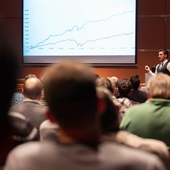 Speaker giving a talk in conference hall at business meeting event. Rear view of unrecognizable people in audience at the conference hall. Business and entrepreneurship concept.