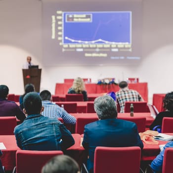 Speaker Giving a Talk at Business Meeting. Audience in the conference hall. Business and Entrepreneurship. Focus on unrecognizable people from rear.