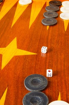 Old varnished wooden board game with plastic checkers and dice. Selective focus with shallow depth of field.