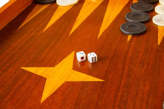 Old varnished wooden board game with plastic checkers and dice. Selective focus with shallow depth of field.