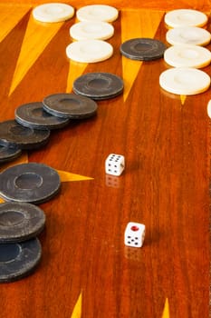 Old varnished wooden board game with plastic checkers and dice. Selective focus with shallow depth of field.