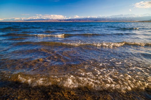 Ultra-wide angle view of small waves on mountain lake at sunny day. Low angle view. Real life photo.