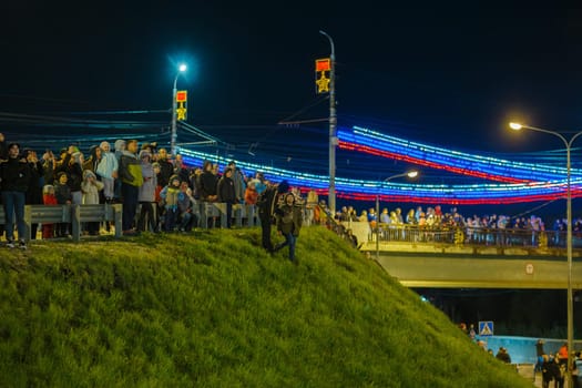 crowd of Russian people at road on the hill and bridge are watching fireworks in a night sky in Tula, Russia - May 9, 2021
