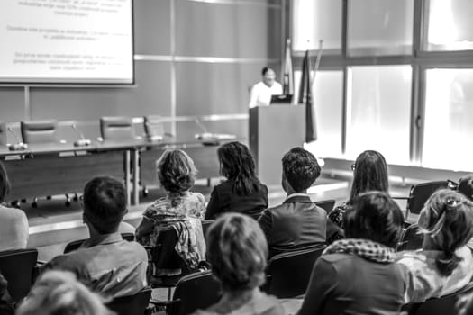 Female speaker giving presentation in lecture hall at university workshop. Audience in conference hall. Rear view of unrecognized participant in audience. Scientific conference event.