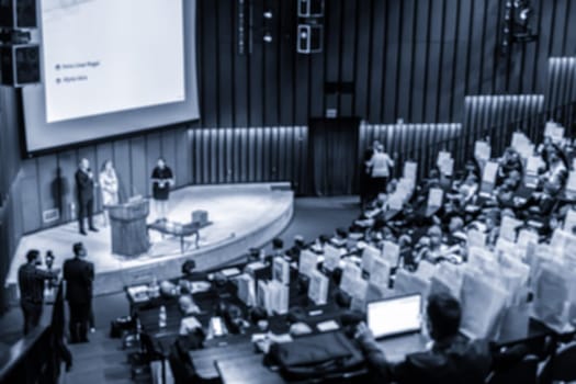 Defocused image of speakers giving a talk at business meeting. Audience in the conference hall. Business and Entrepreneurship concept. Blue toned.