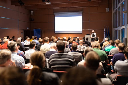 Speaker giving a talk in conference hall at business meeting event. Rear view of unrecognizable people in audience at the conference hall. Business and entrepreneurship concept.