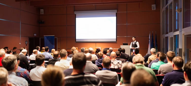 Speaker giving a talk in conference hall at business meeting event. Rear view of unrecognizable people in audience at the conference hall. Business and entrepreneurship concept.