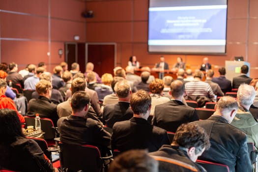 Business and entrepreneurship symposium. Speaker giving a talk at business meeting. Audience in the conference hall. Rear view of unrecognized participant in audience.