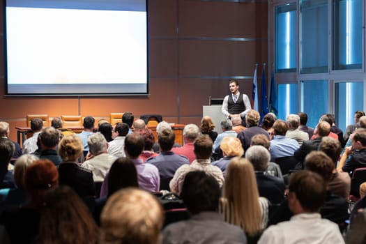 Speaker giving a talk in conference hall at business meeting event. Rear view of unrecognizable people in audience at the conference hall. Business and entrepreneurship concept.