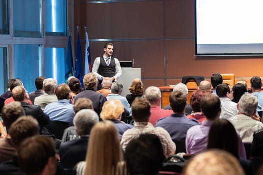 Speaker giving a talk in conference hall at business meeting event. Rear view of unrecognizable people in audience at the conference hall. Business and entrepreneurship concept.