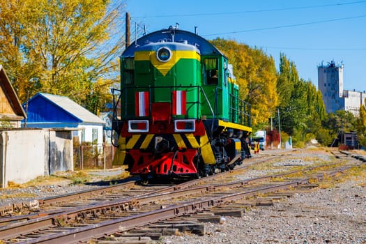 green diesel locomotive moving near small Asian Balykchy town at summer day in Kyrgyzstan.