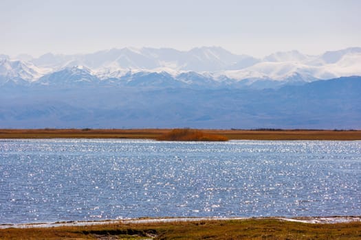 Blue calm water in Issyk-Kul lake with mountains on background at autumn afternoon.