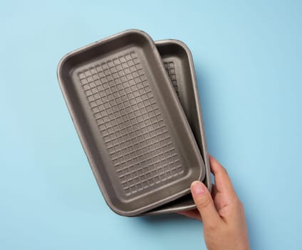 Hand holds black disposable polystyrene foam rectangular plate for packaging vegetables and meat on a blue background, top view