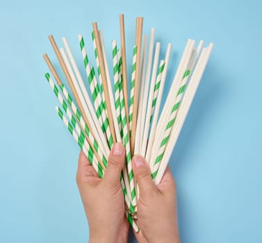 Female hand holding paper cocktail straws on a blue background