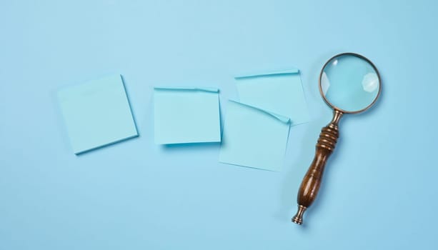 Wooden magnifying glass and paper blue stickers on a blue background