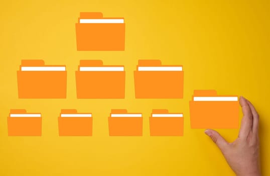 Hand holds a yellow folder over a yellow background with several folders. Concept of control and systematization of documents
