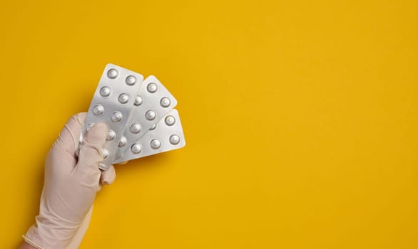 Female hand holding round pills in a blister pack on a yellow background, top view. Copy space