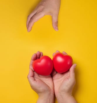 Woman's hand holding a red heart on a yellow background. Donation and kindness concept