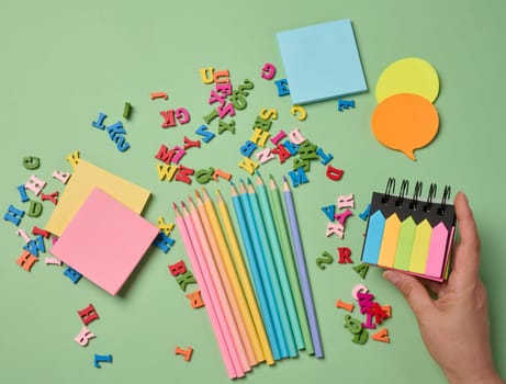 Stationery laid out on a green background. Multi-colored pencils ,  sticky notes and wooden letters, preparing for study or work, organizing workspace