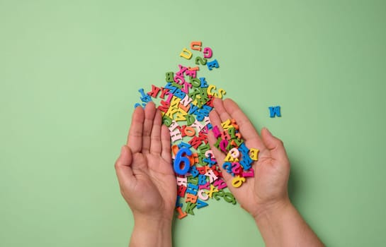 Two female hands and scattered wooden letters of the English alphabet on a green background
