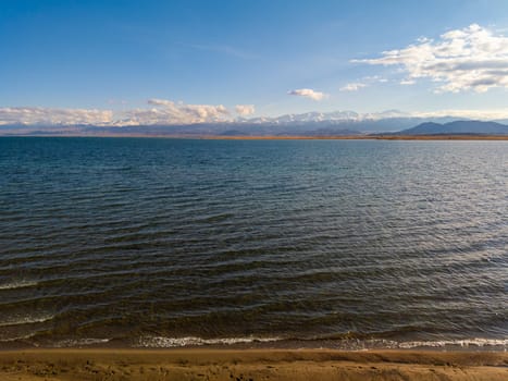 Blue calm water in Issyk-Kul lake with mountains on background at autumn afternoon.