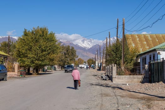 senior woman walking down the street of small Kyrgyz town at sunny autumn day in Balykchy, Kyrgyzstan- October 21, 2022