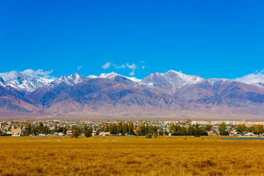 Small Kyrgyz town Balykchy cityscape in front of massive mountain ridge at sunny autumn afternoon