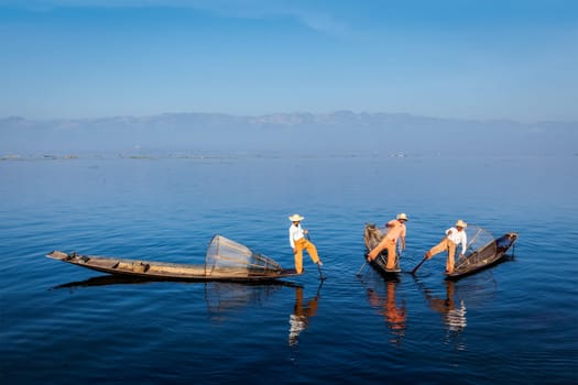 Myanmar travel attraction landmark - Traditional Burmese fishermen with fishing nets on boats at Inle lake in Myanmar famous for their distinctive one legged rowing style