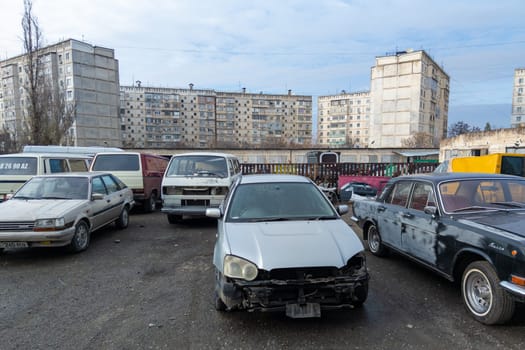 old used cars waiting for repairs in front of old soviet high-rise apartment buildings in Bishkek, Kyrgyzstan - December 21, 2022