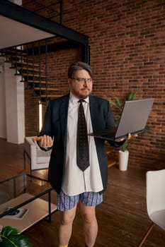 Funny businessman in formal suit and underwear giving self presentation online standing in living room. Freelance business, home office and successful remote job occupation