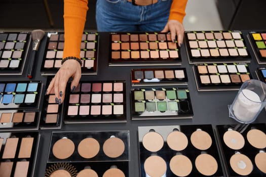 Lady choosing eye shadow palette in cosmetics shop. Many different colors of decorative products for face
