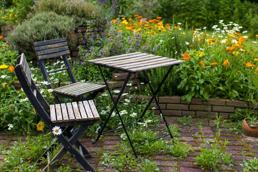 wild garden - herb spiral in the garden with fresh herbs and flowers, table and chair