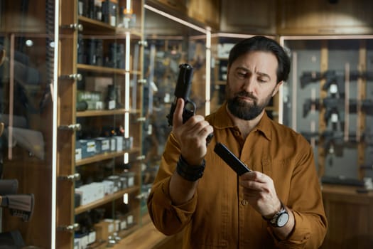 Portrait of salesman charging handgun demonstrating new model for customer standing over shop store showcase