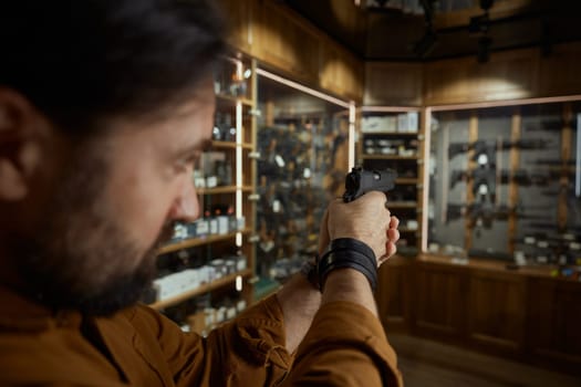 Man aiming the handgun while choosing weapon in shop. Closeup view on aiming gunpoint selective focus