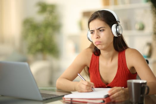 Frustrated student wearing headphone blowing listening online lesson at home