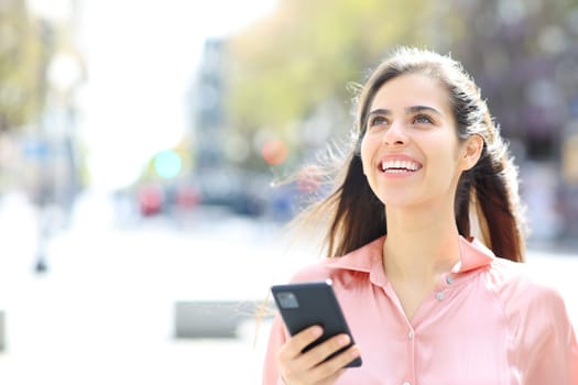 Happy woman laughing holding phone in the street looking up