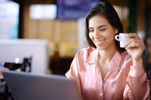 Happy elegant woman in a bar working with laptop and holding cup