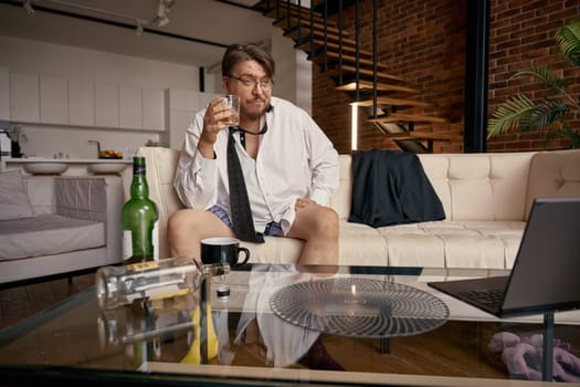 Frustrated drunk businessman working online having troubles with alcohol. Male boss entrepreneur discussing digital project remotely during virtual business meeting. Career and alcoholism