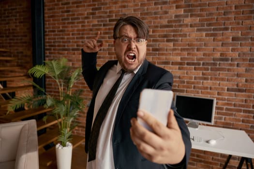 Crazy boss mad businessman shouting on mobile phone having bad conversation with employee or coworker. Angry male entrepreneur working remotely feeling displeasure