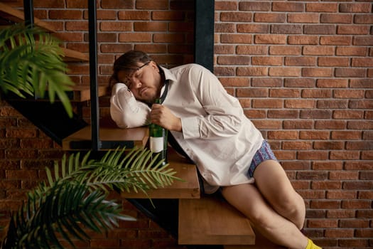 Depressed drunken businessman freelancer suffering from professional crisis, having financial problems and going through bankruptcy sitting on home staircase