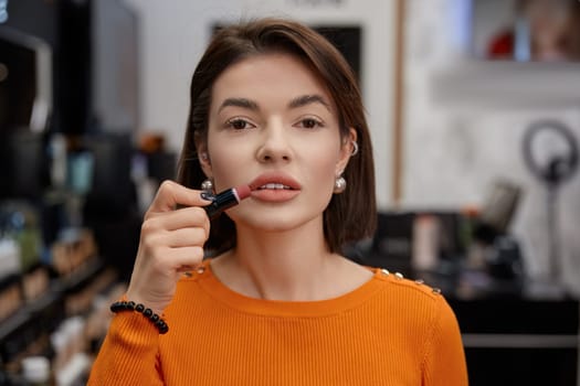 Woman testing matt lipstick, her face close up. Lady's lips in cosmetics store