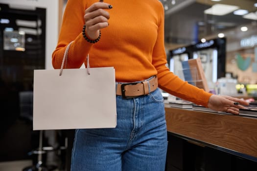 Young woman shopping in cosmetics store with paper bag. Attractive lady choosing decorative cosmetics